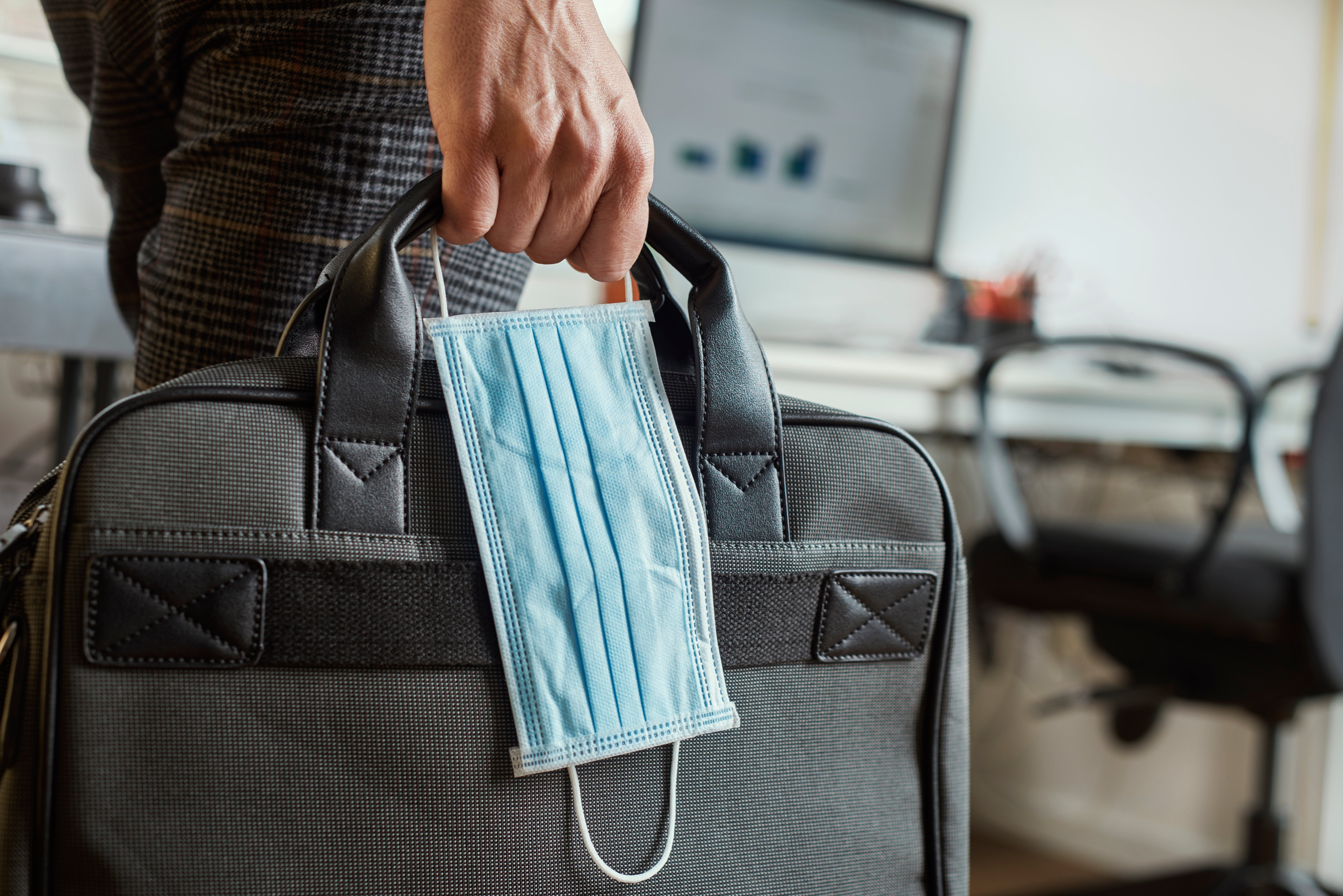 A man with a mask carries his briefcase into the office as he works safely in an office setting